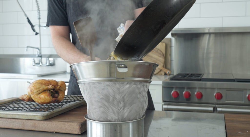 Chef using a large chinois to strain the chicken gravy