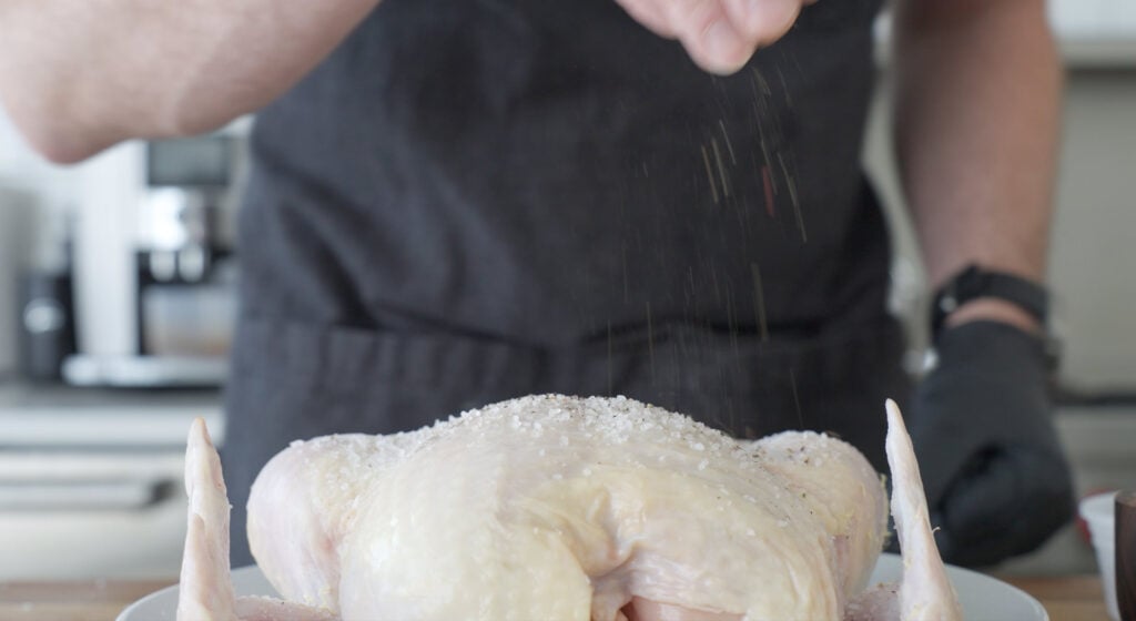 chef sprinkling salt on whole chicken