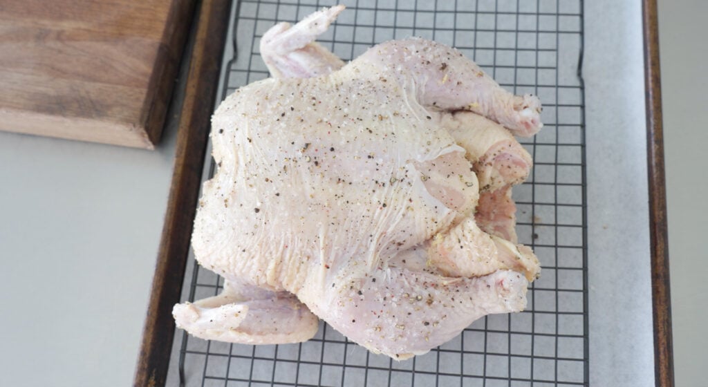 whole seasoned chicken on a rack over a pan