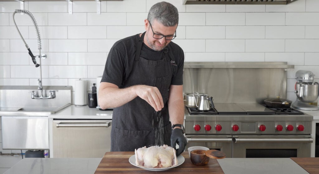 Chef seasoning chicken with salt and pepper