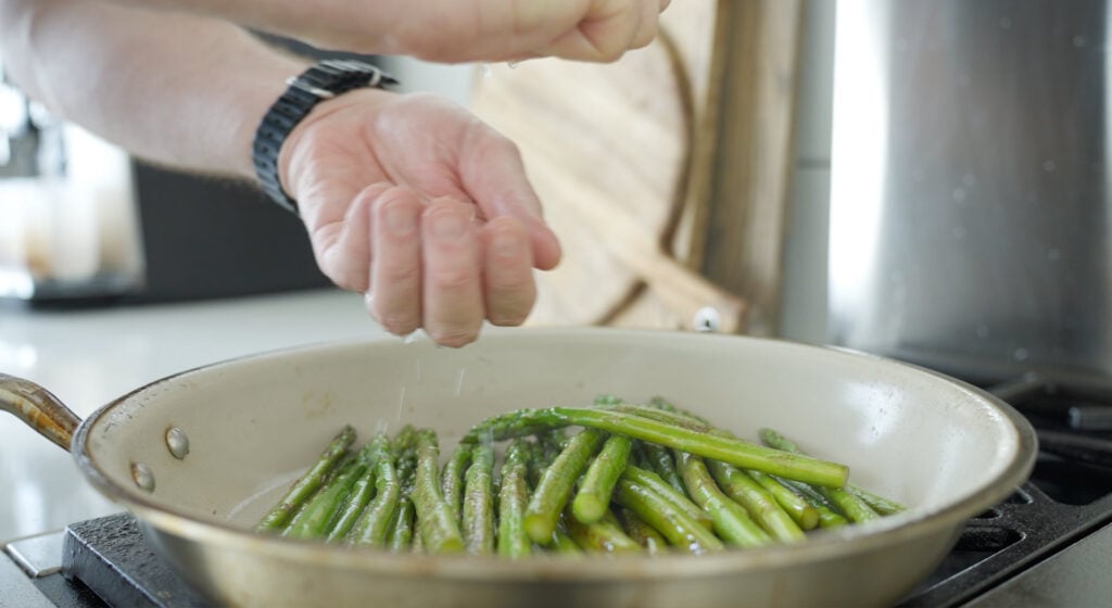 lemon being squeezed over asparagus in pan