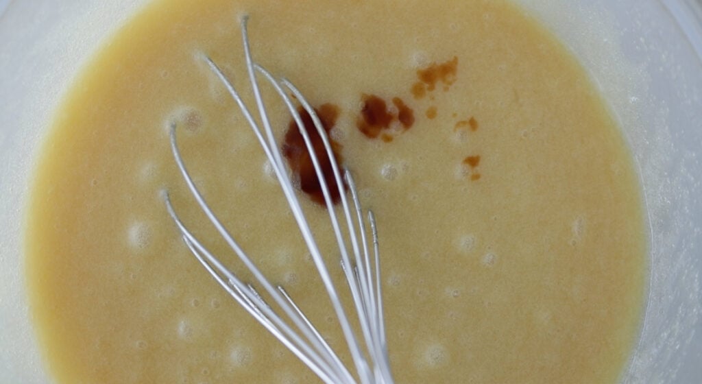 whisking vanilla extract into a bowl of melted butter and eggs