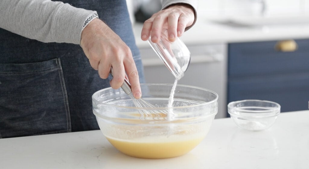 pouring cinnamon and baking powder into a bowl with mashed bananas