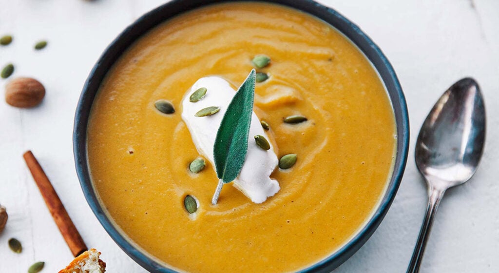 a black bowl full of butternut squash soup with a fresh sage leaf