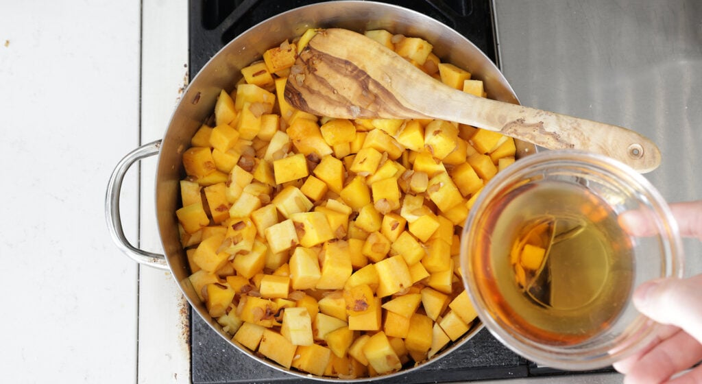 cubed butternut squash in a pot with a glass of bourbon