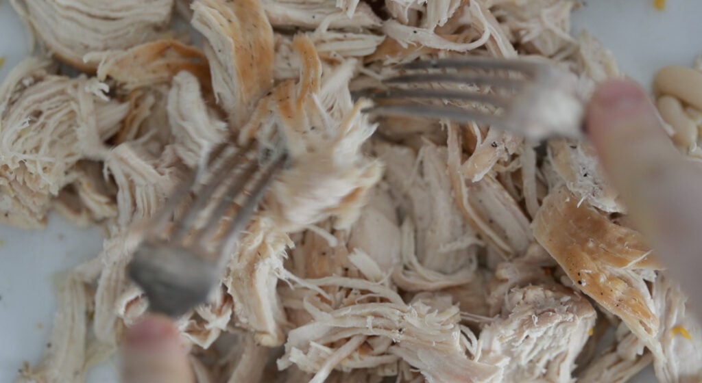cooking the soup with chicken stock and shredding the chicken