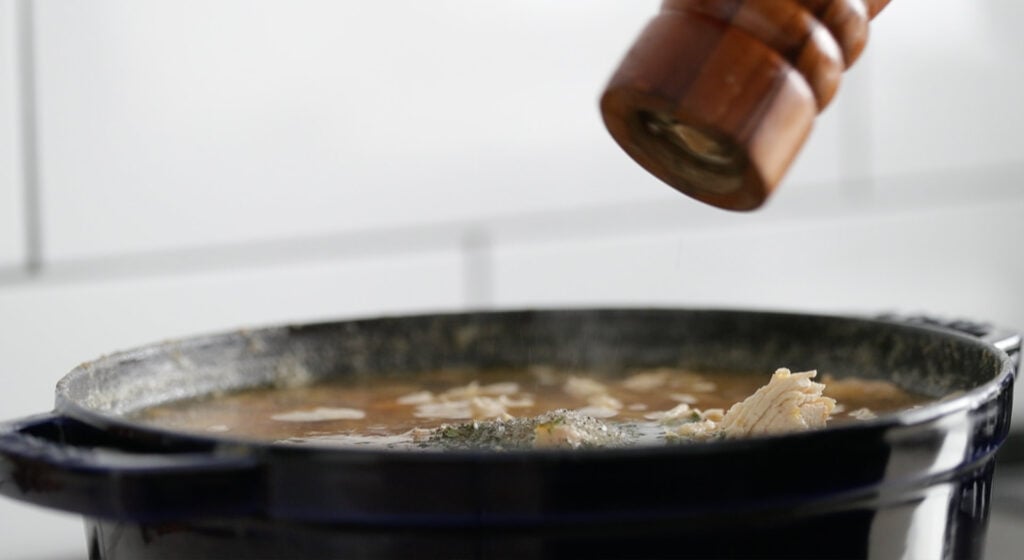 adjusting the seasonings of a soup with salt and pepper
