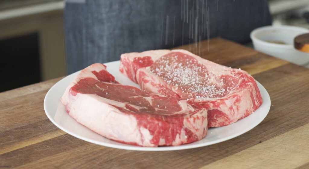 Seasoning 2 Ribeyes on a plate with salt