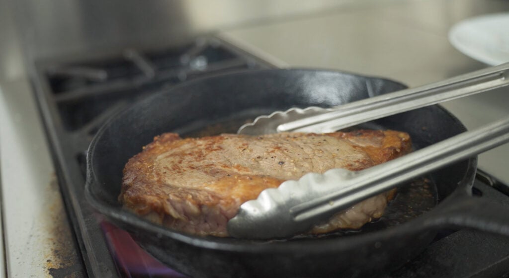 using tongs to turn browned ribeye over