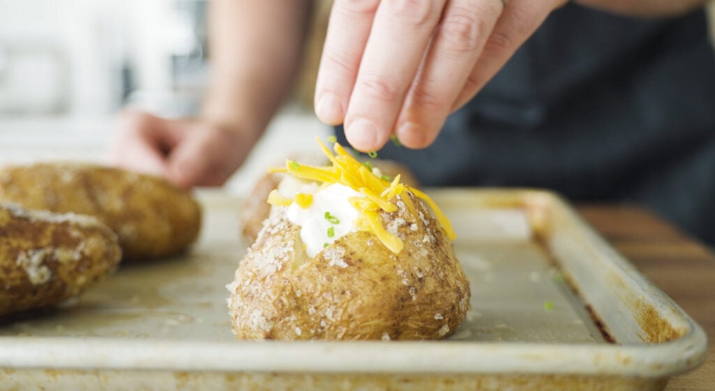 adding chives and other toppings to the cut potato