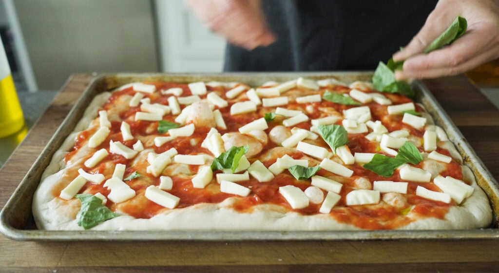 pizza ingredients added to top of focaccia dough