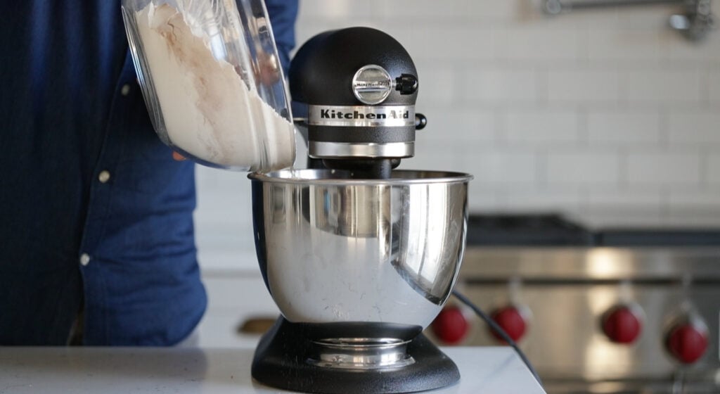Pouring flour mixture into a mixer bowl.