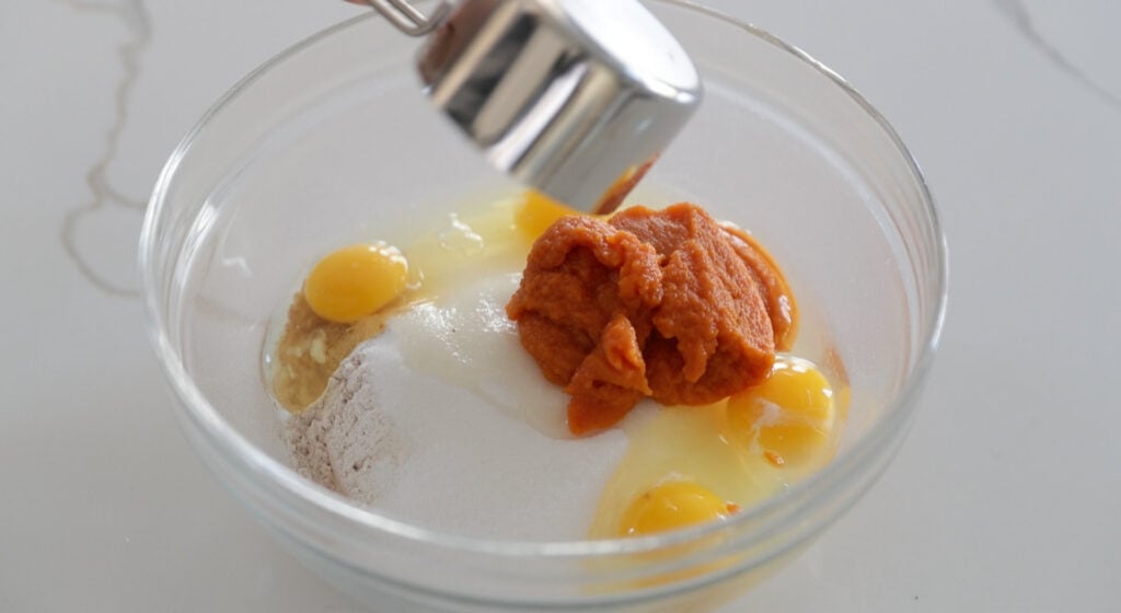 mixing eggs in a bowl with pumpkin and flour