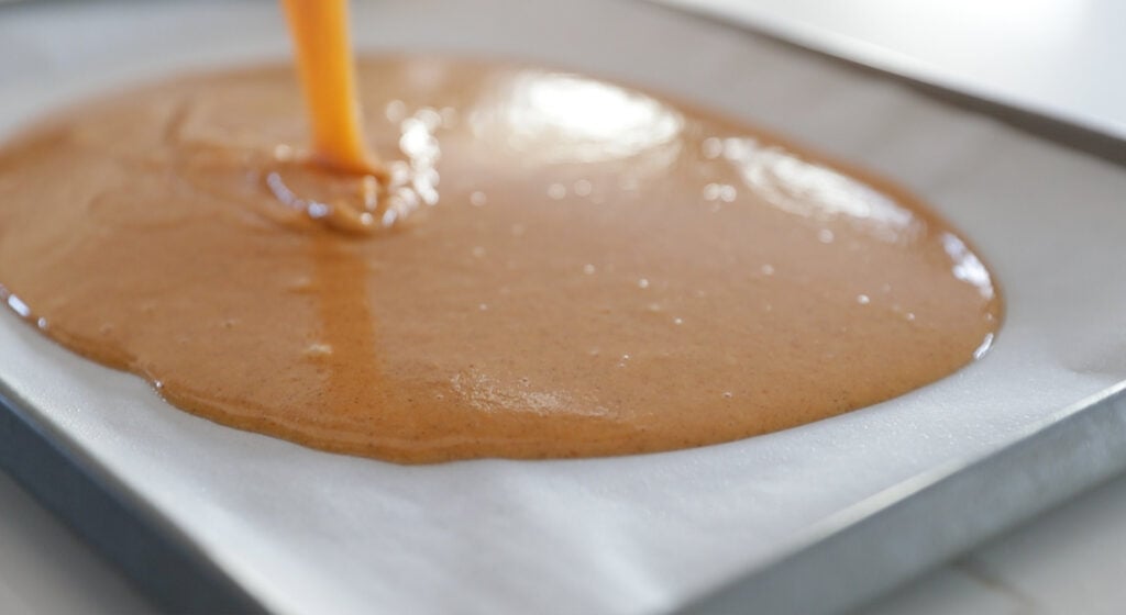 adding pumpkin batter to a sheet tray with parchment paper