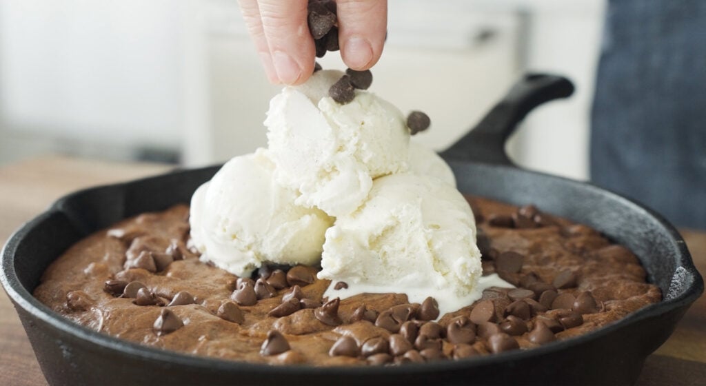 vanillya ice cream and chocolate chips being added to skillet brownie