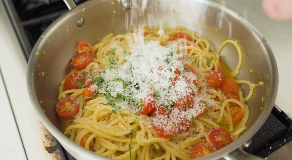 adding cheese to tomato basil pasta