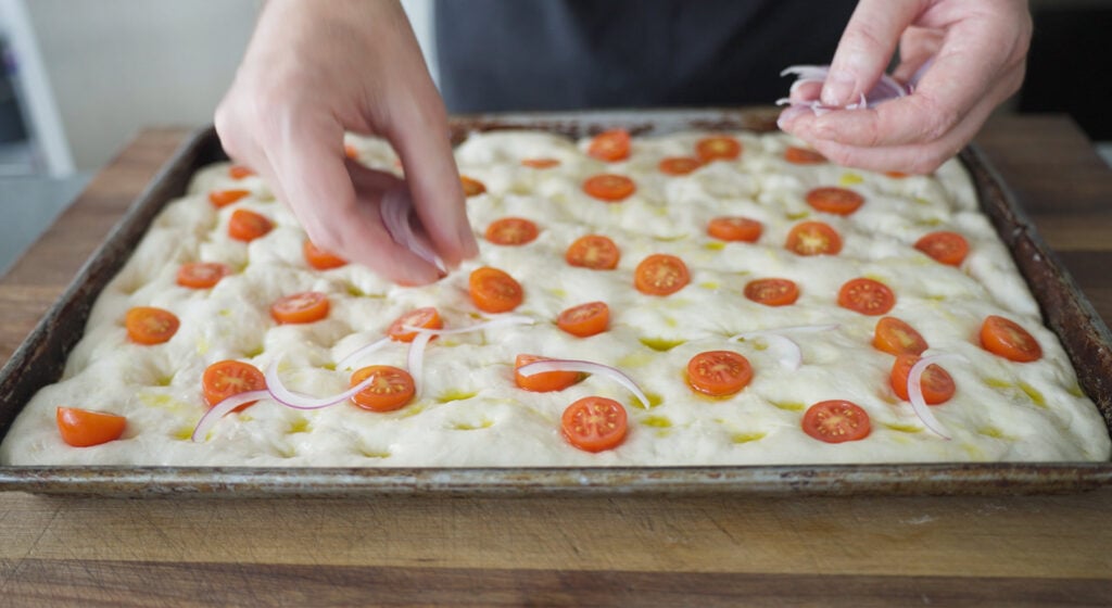 tomatoes being placed on dough in pan