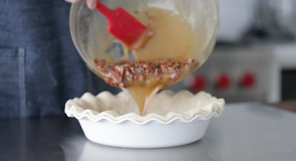 pouring pecan pie filling into a pie crust
