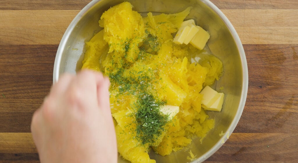 Adding finishing ingredients to pot with squash