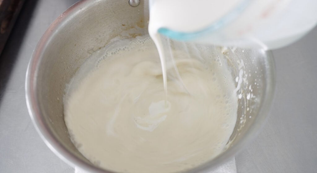 Pouring heavy cream into mixture in sauce pan