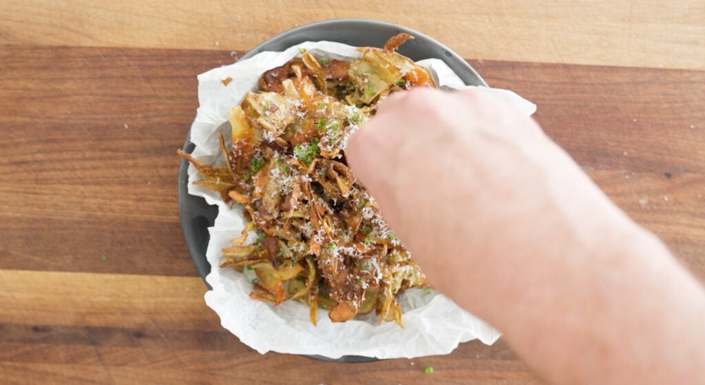 Potato skins in a serving bowl being topped with cheese