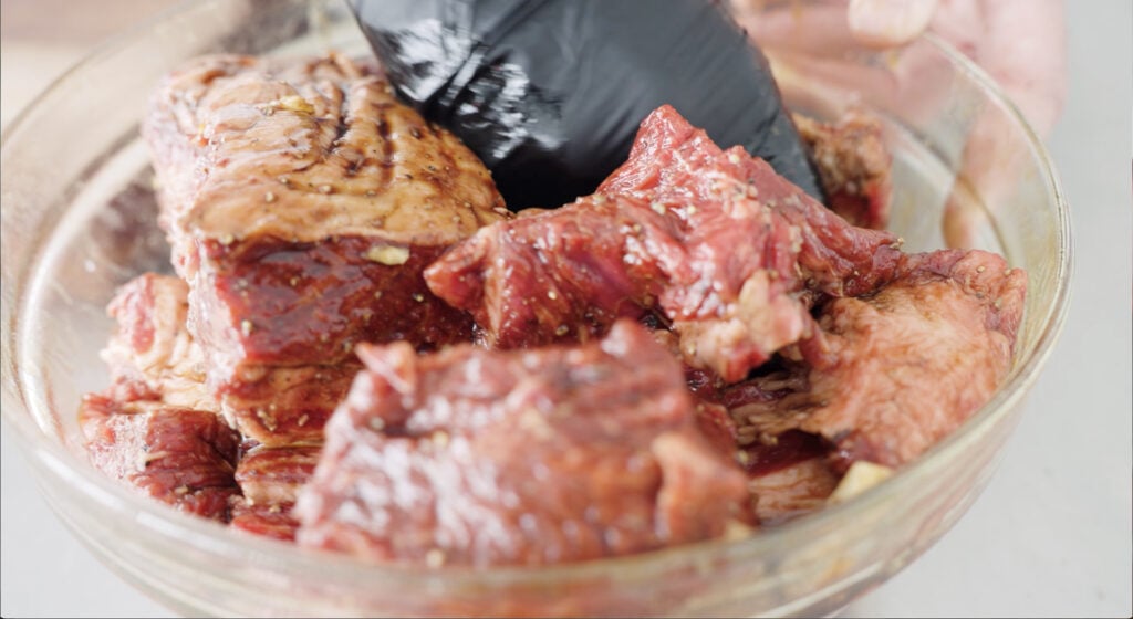 Beef being mixed with marinade ingredients in a bowl