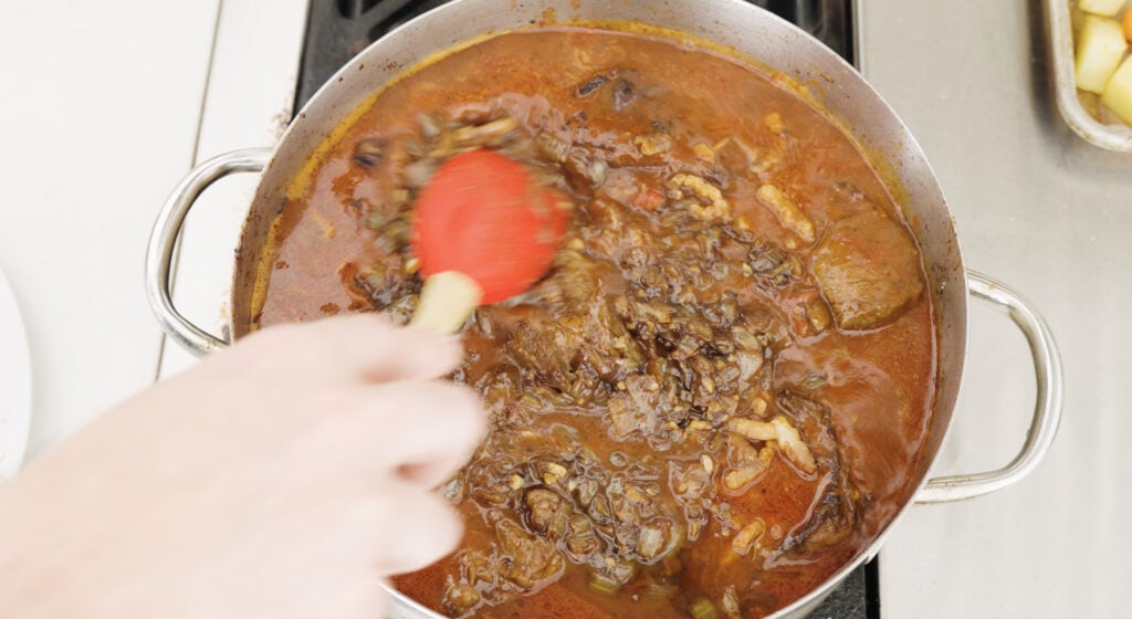 Beef being added to pot of sauce