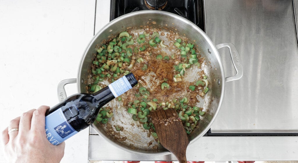 Hand pouring sherry into the pot with the cellery and shallots