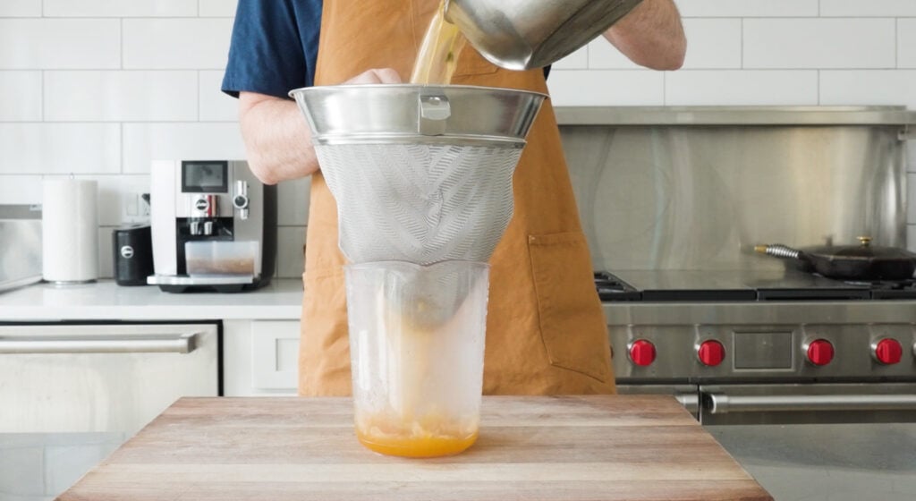 Pouring shrimp stock into a chinois over a large container