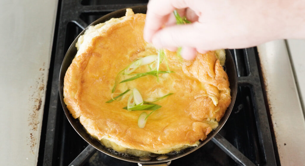 Adding sliced green onions to cooked thai omelette in a pan