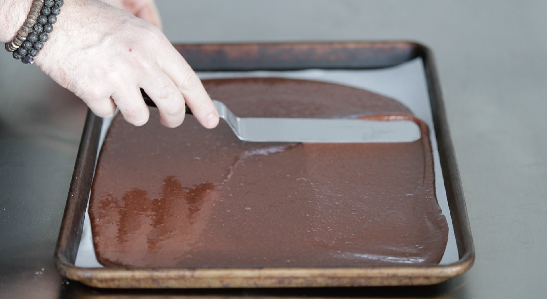 spreading a chocolate batter on a sheet tray