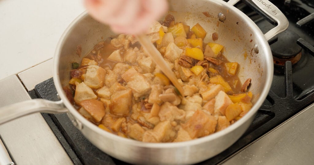 Using a wooden spoon to stir the soaked bread into the ingredients in the pot.