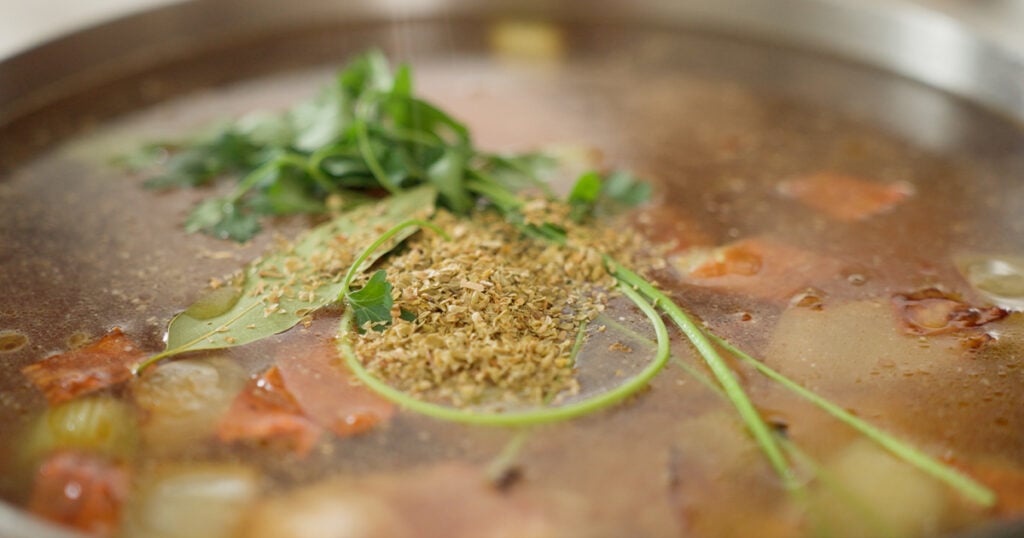 parsley, dried oregana and bay leaf floating on top of the ingredients in the pot