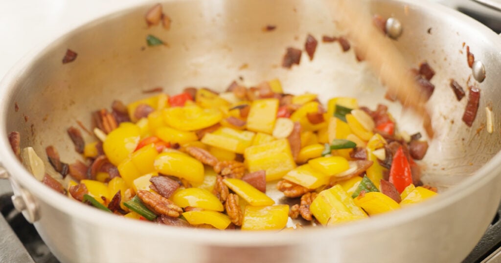 Close up of the onions, peppers, garlic and pecans cooking in a pan