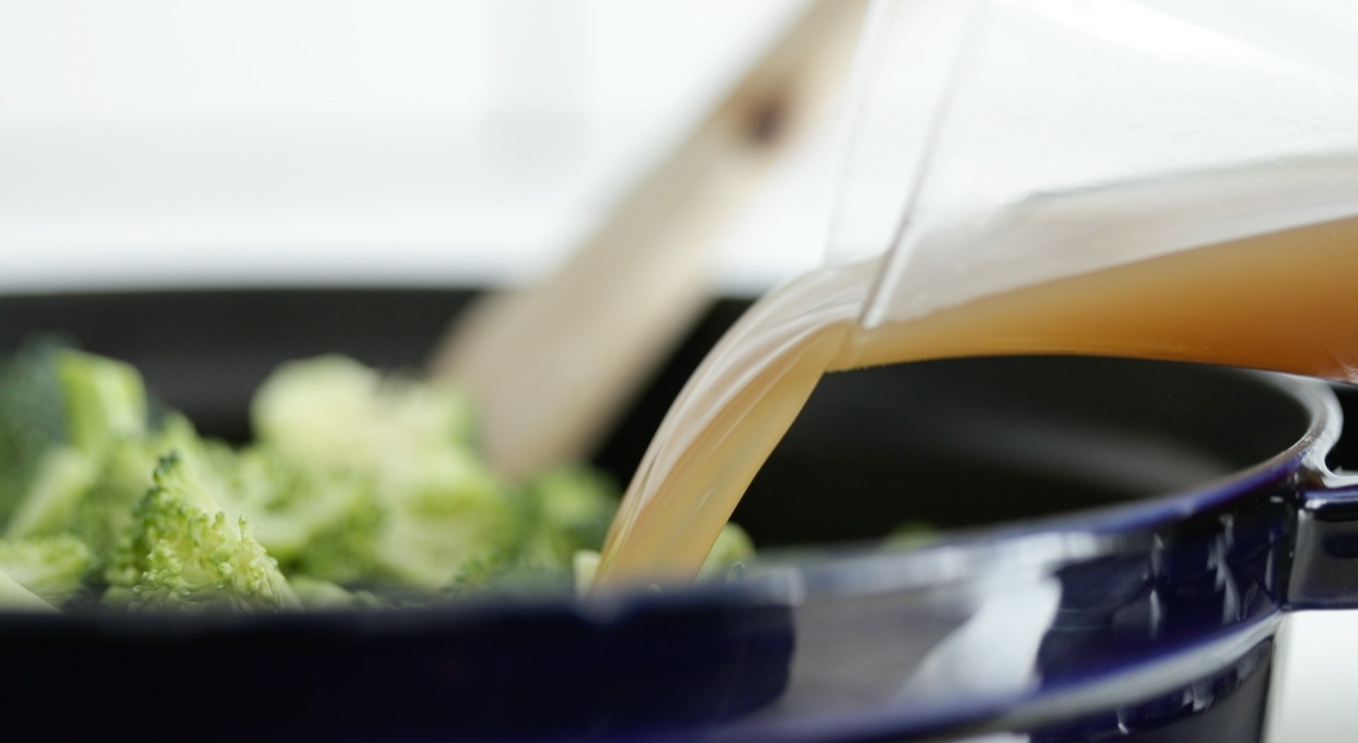 adding chicken stock to a pot with broccoli