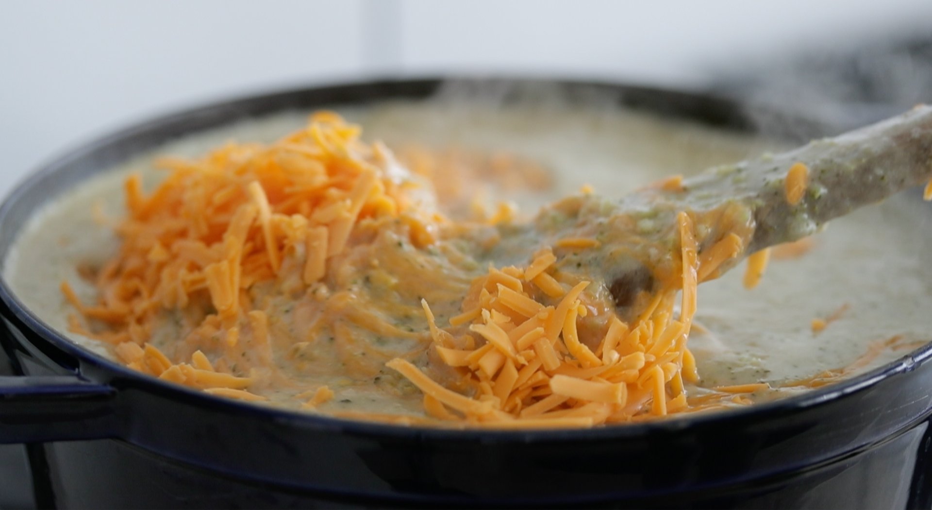 adding cheddar cheese to a broccoli soup
