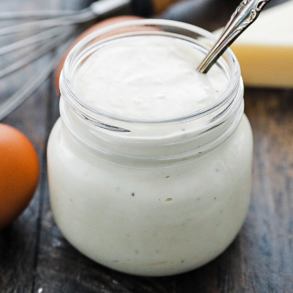 pouring in grated parmesan cheese to caesar salad dressing in a food processor