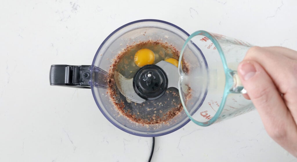 adding eggs and lemon juice to a food processor with anchovies and garlic