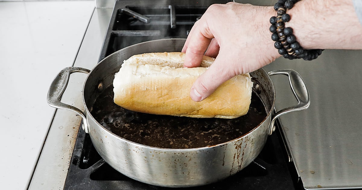 dipping the bottom part of a bun in hot au jus