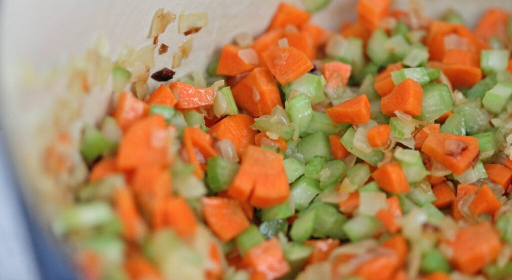 mixing onions, celery, and carrots with flour to make a roux