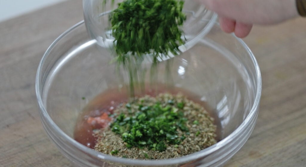 adding fresh herbs to a bowl with red wine vinegar