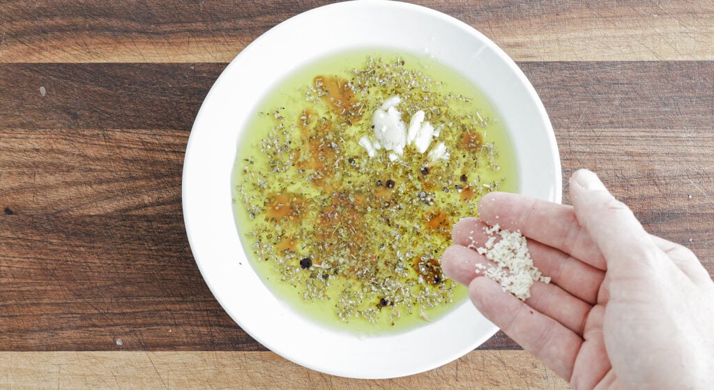 Adding cheese to olive oil bread dip ingredients on a plate