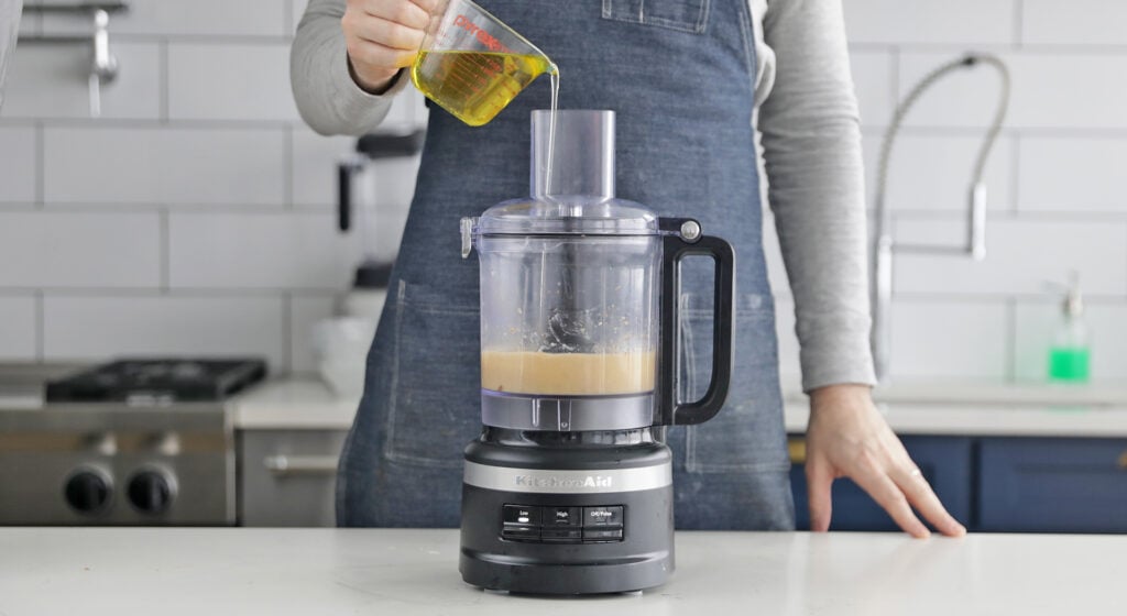 drizzling olive oil to a caesar salad dressing in a food processor
