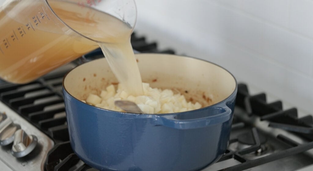 adding chicken stock to a pot of potatoes