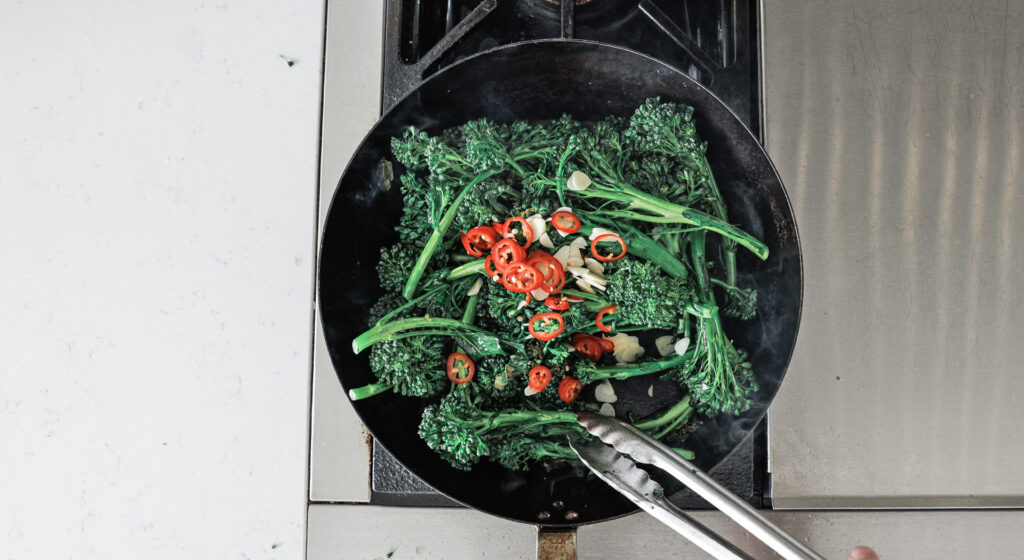 Peppers and garlic added to pan on top of broccoli