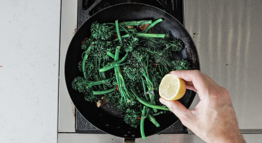 Squeezing a lemon over the sauteed broccolini