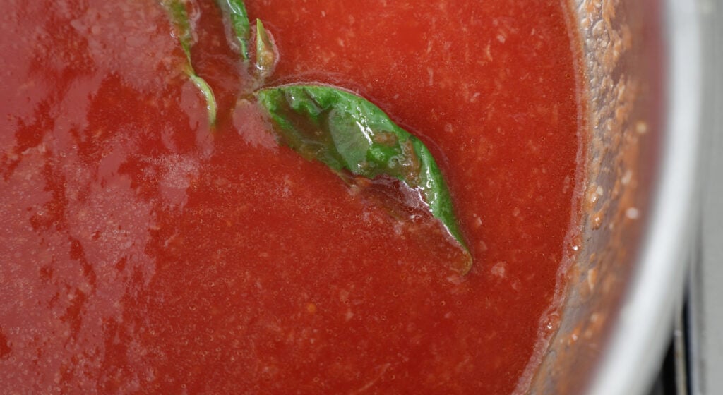 Close up of crushed tomatoes in a pot with basil on top