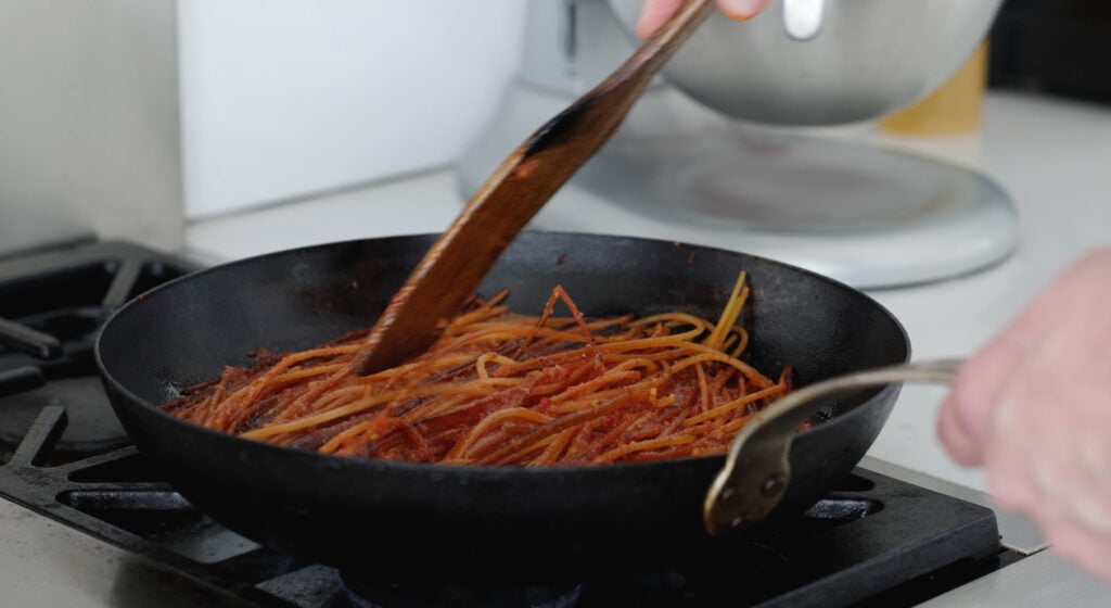  Using a wooden utensile to move Spaghetti in a skillet