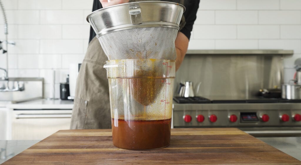 Using a chinois to strain the sauce into a container