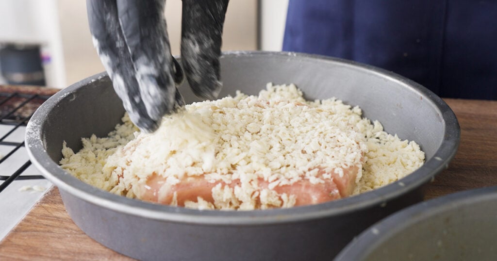 A piece of pork being dipped in panko

